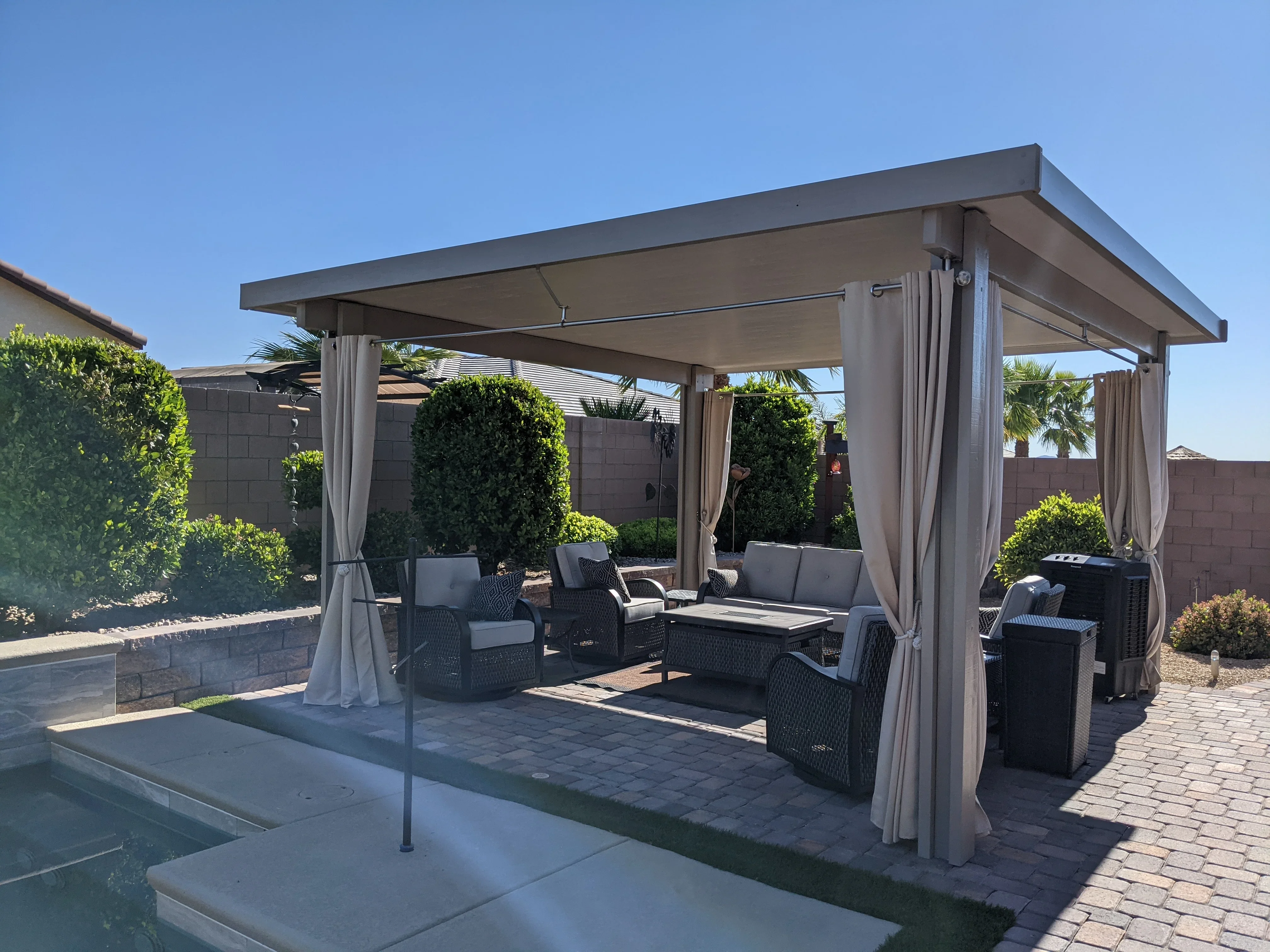 Modern aluminum pergola with retractable curtains over paver patio with seating and pool