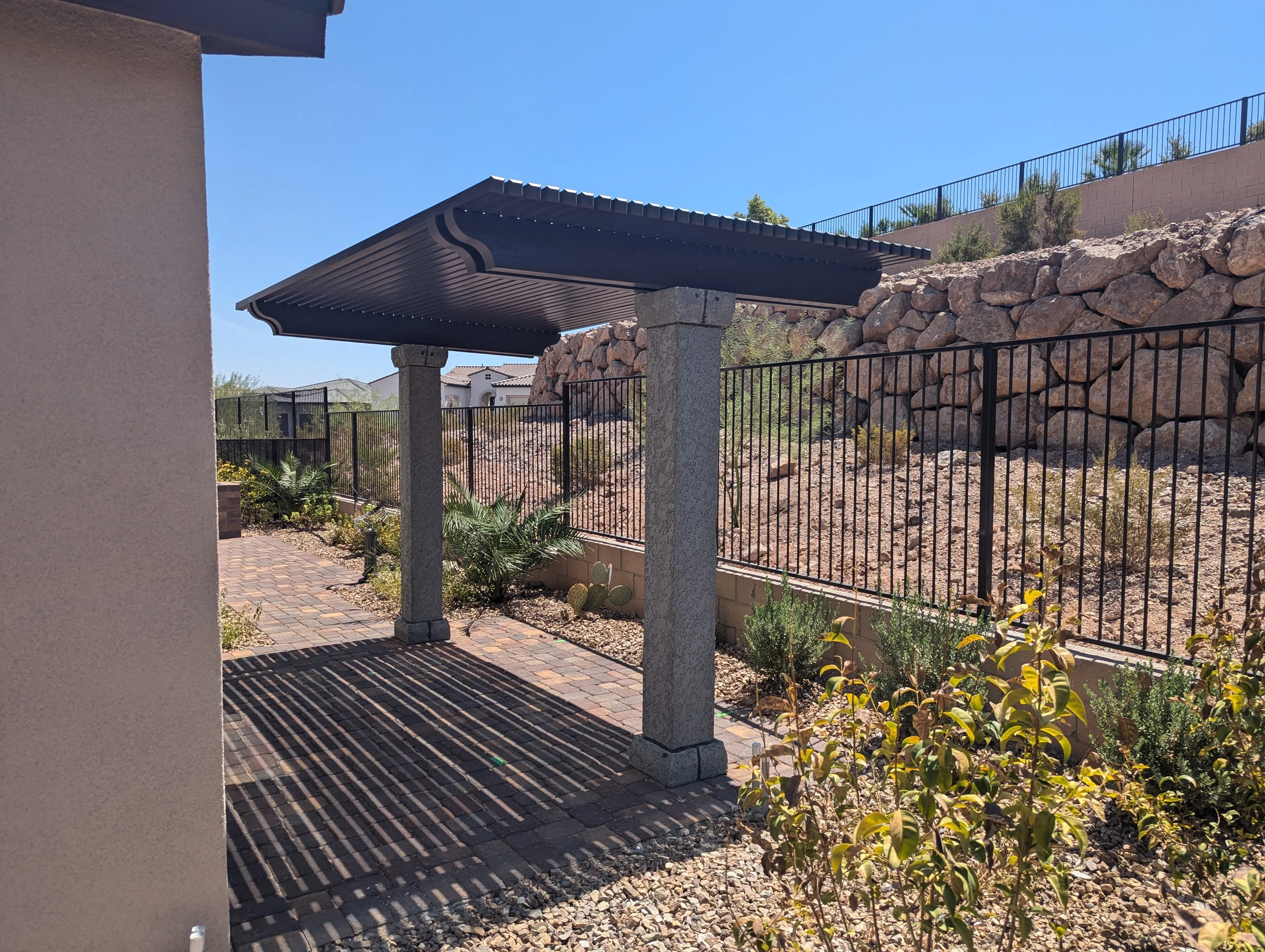 Modern black pergola with louvered roof over brick patio and stone retaining wall