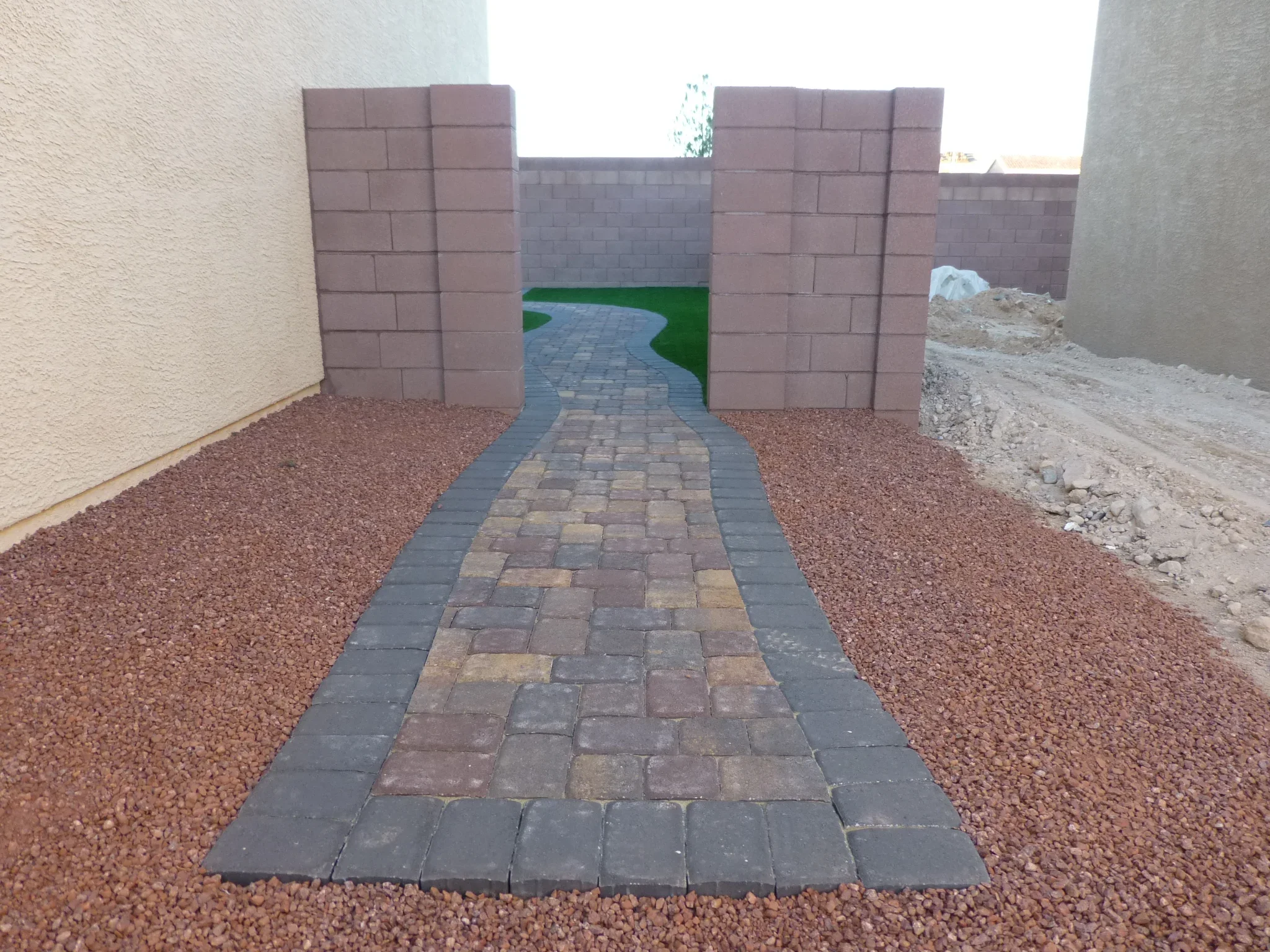 Curved brick paver walkway with river rock borders and concrete block walls in courtyard