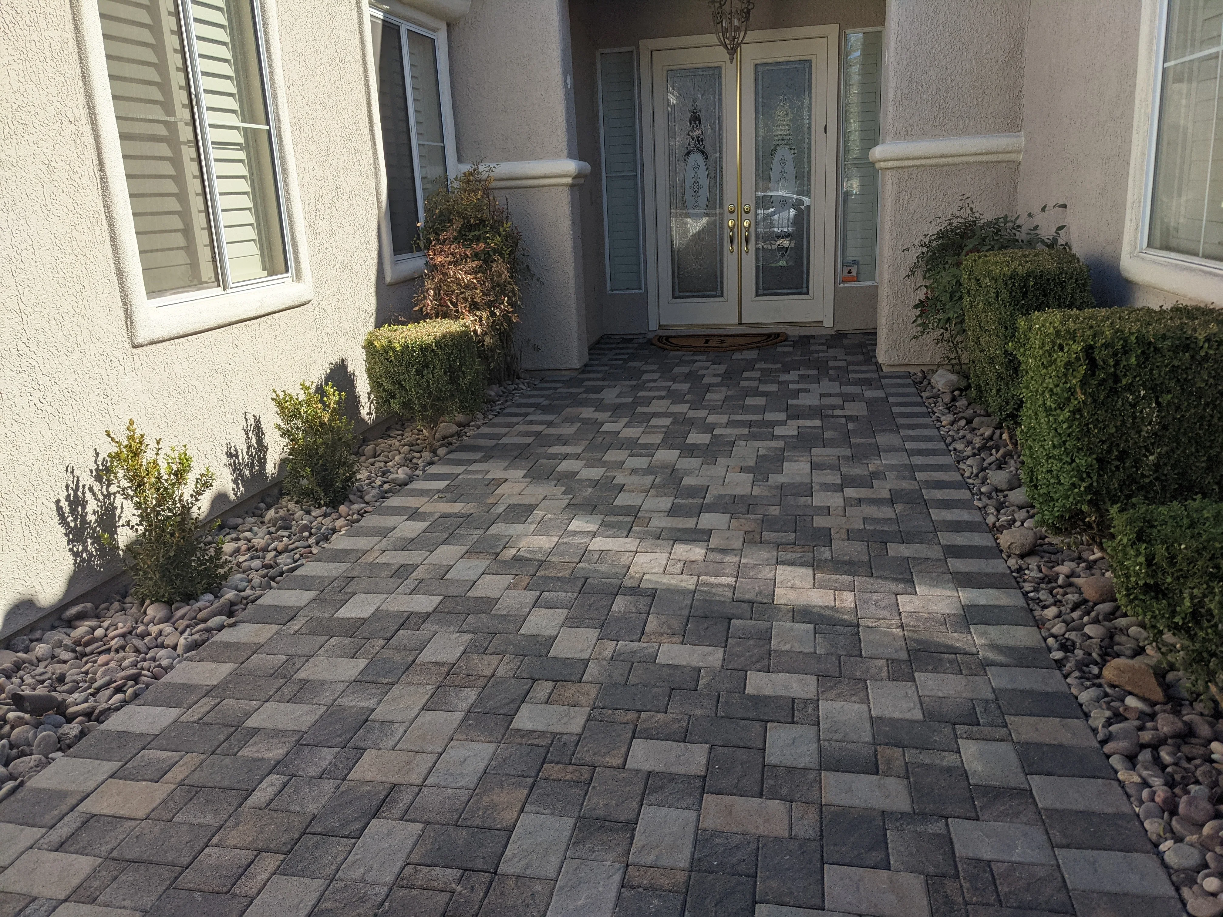 Herringbone paver entryway with charcoal pavers, river rock borders, and green hedges