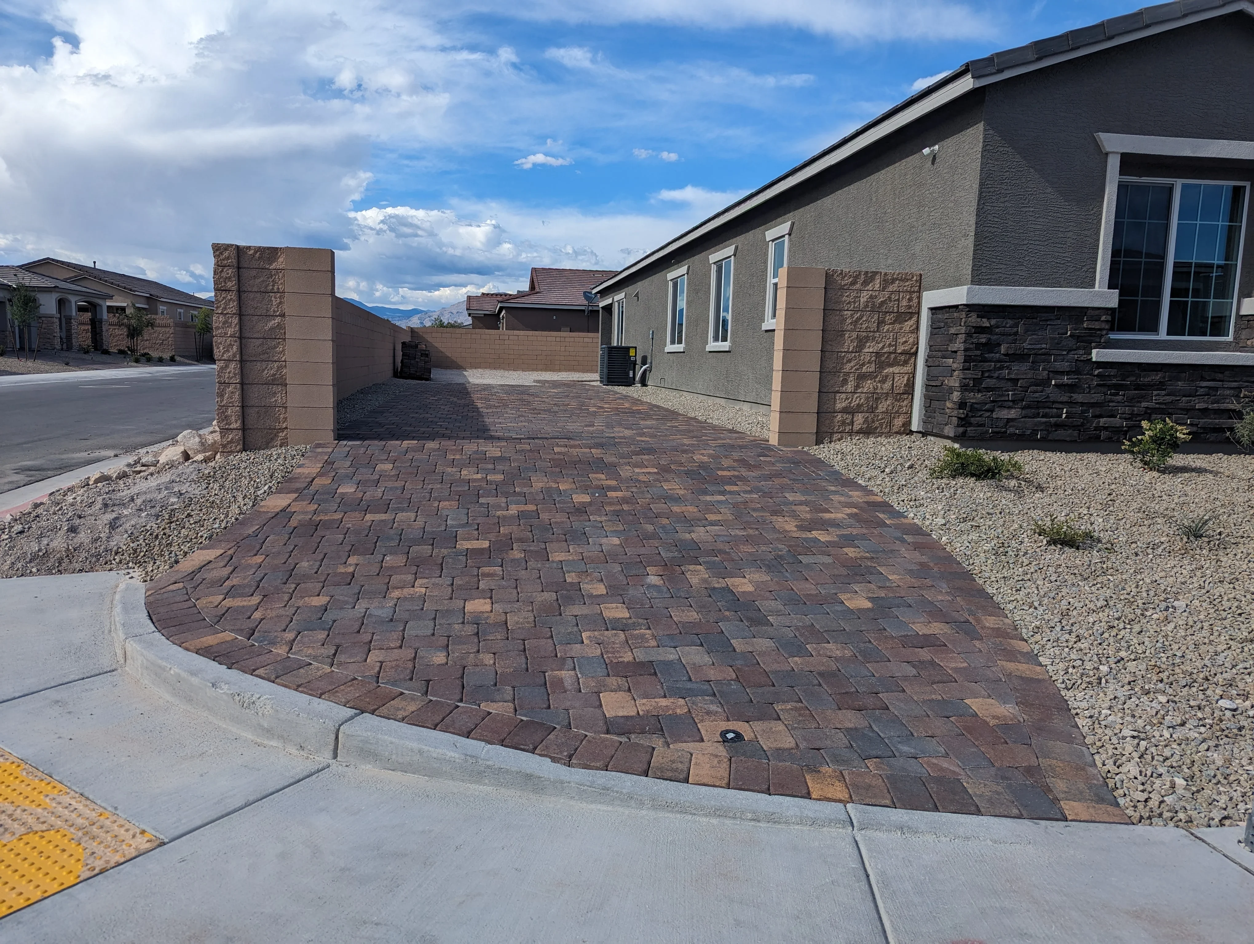 Curved decorative paver driveway with stone pillars leading to modern home