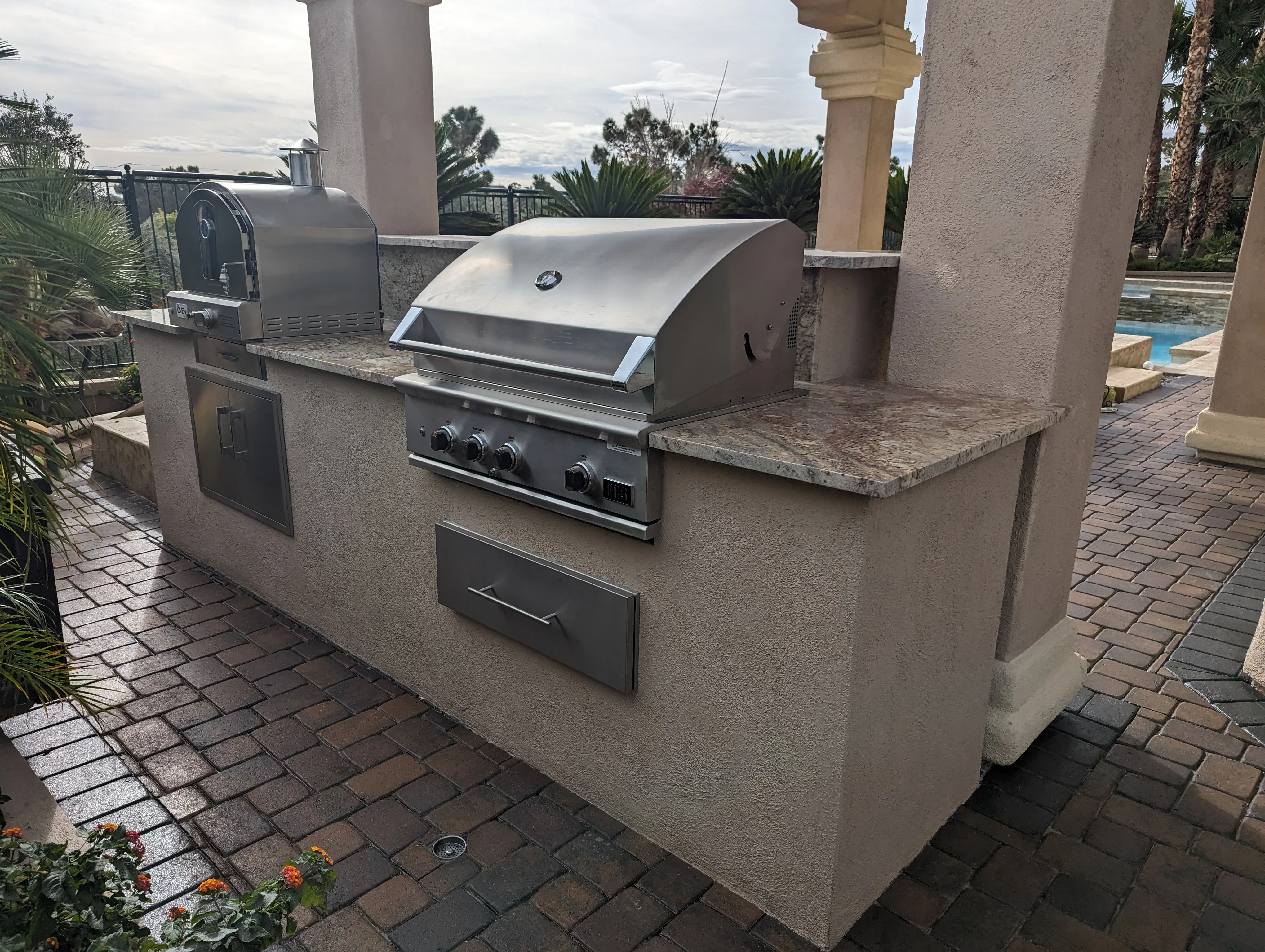 Stucco outdoor kitchen with stainless steel grill and granite counters by pool