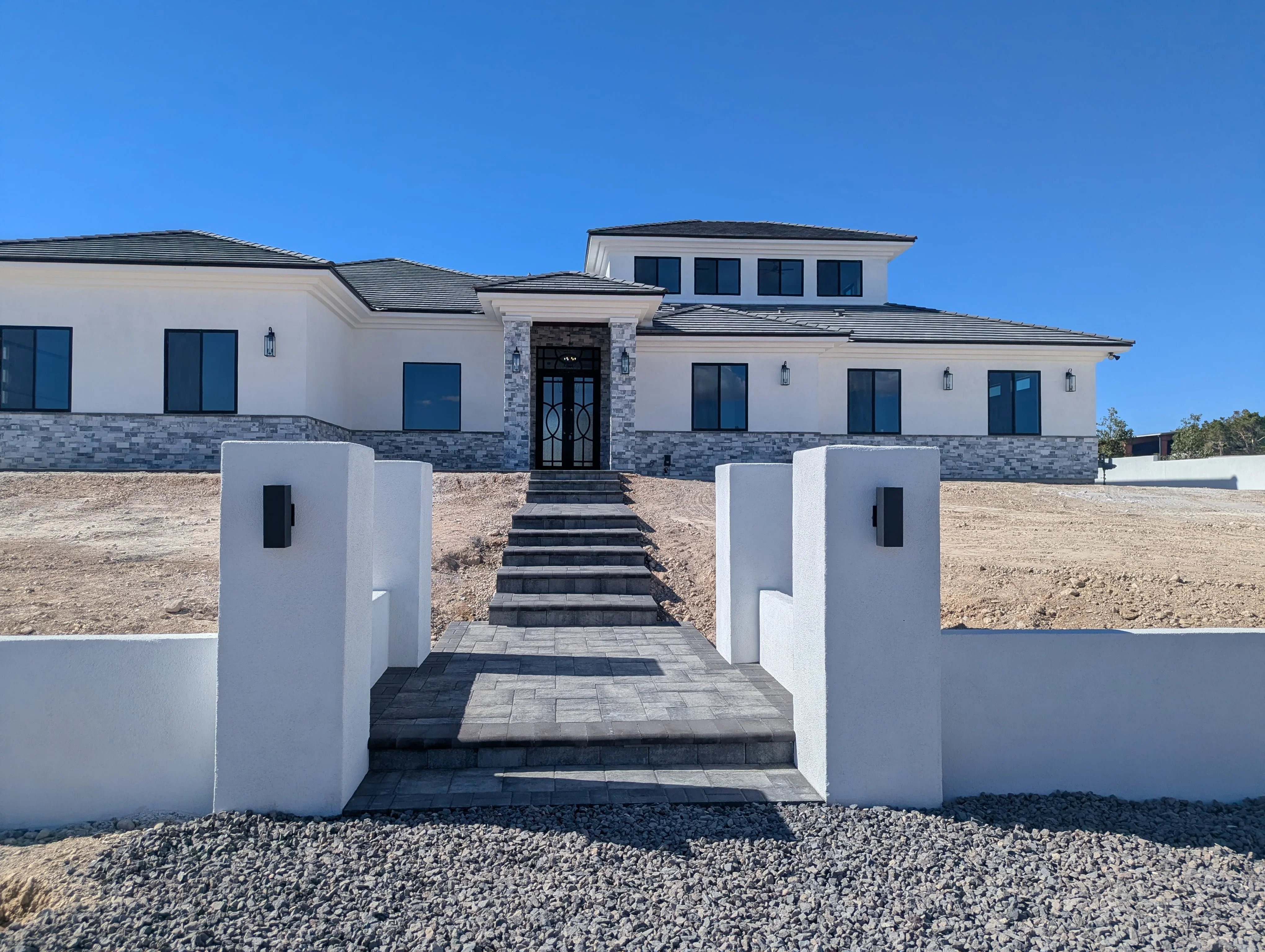 Modern home entry with paver walkway, white stone pillars, and dark stone steps