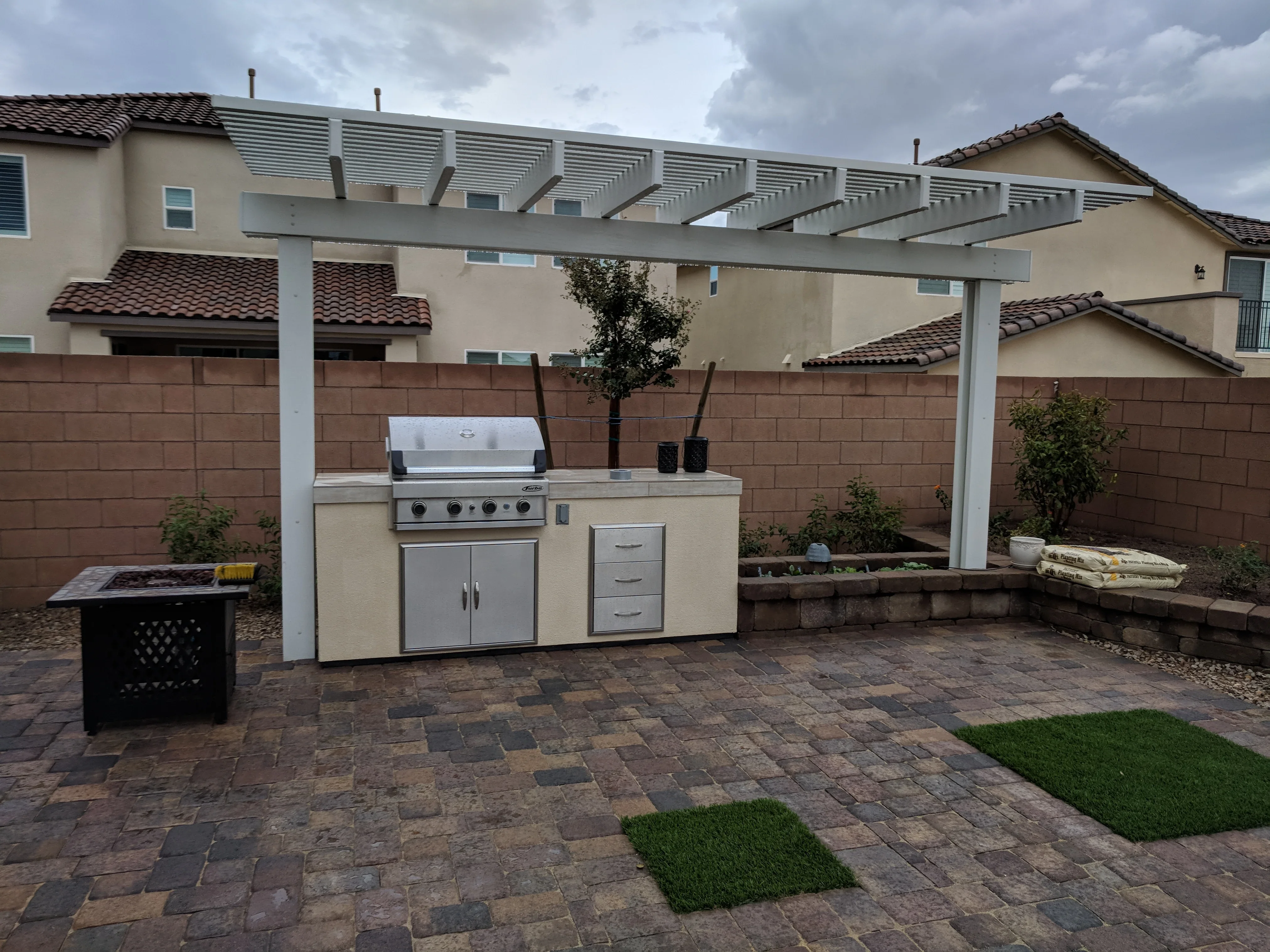 Outdoor kitchen with pergola, gas grill, and paver patio in residential backyard