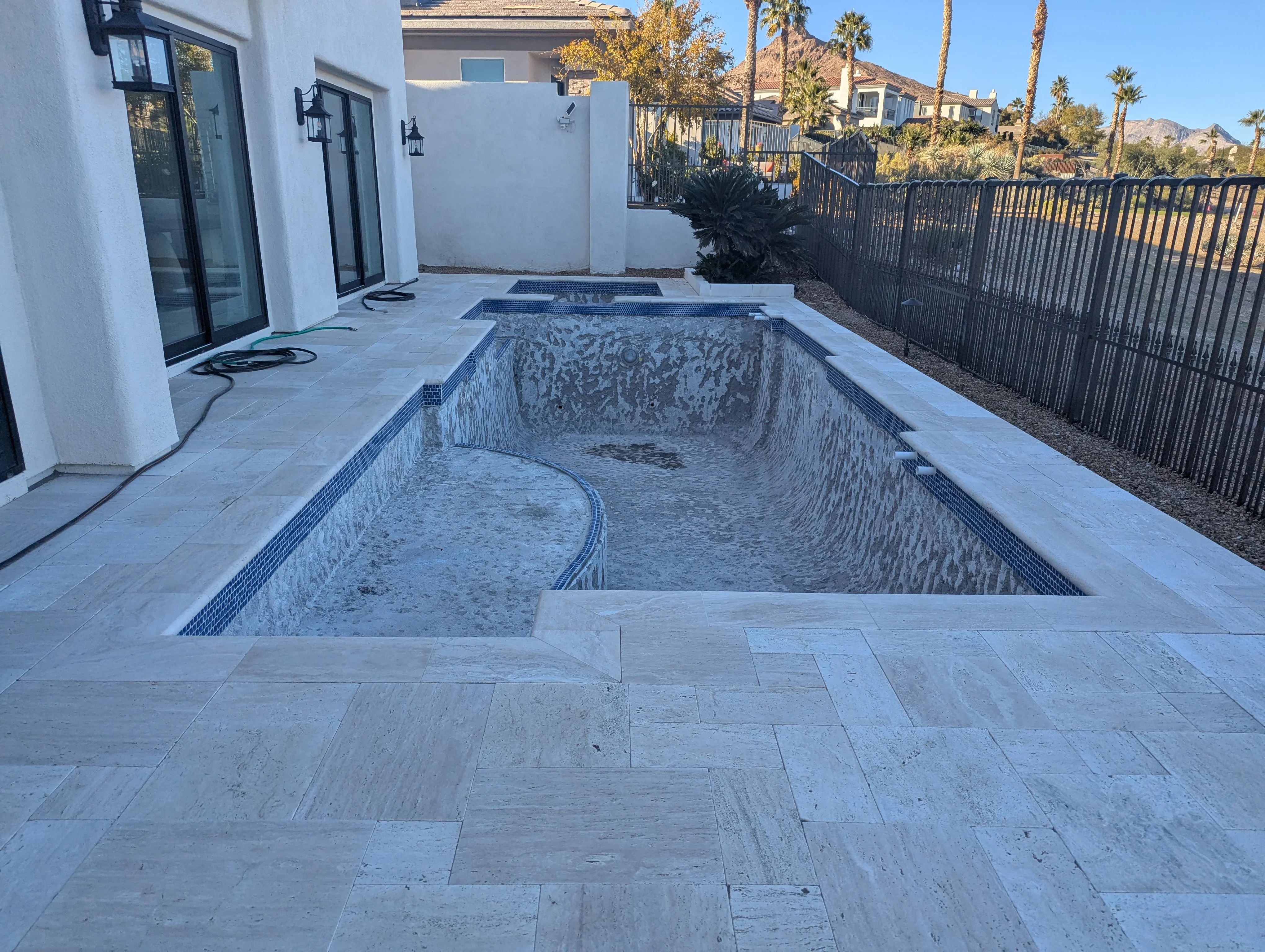 Newly built pool with travertine deck and black metal fencing in Las Vegas backyard