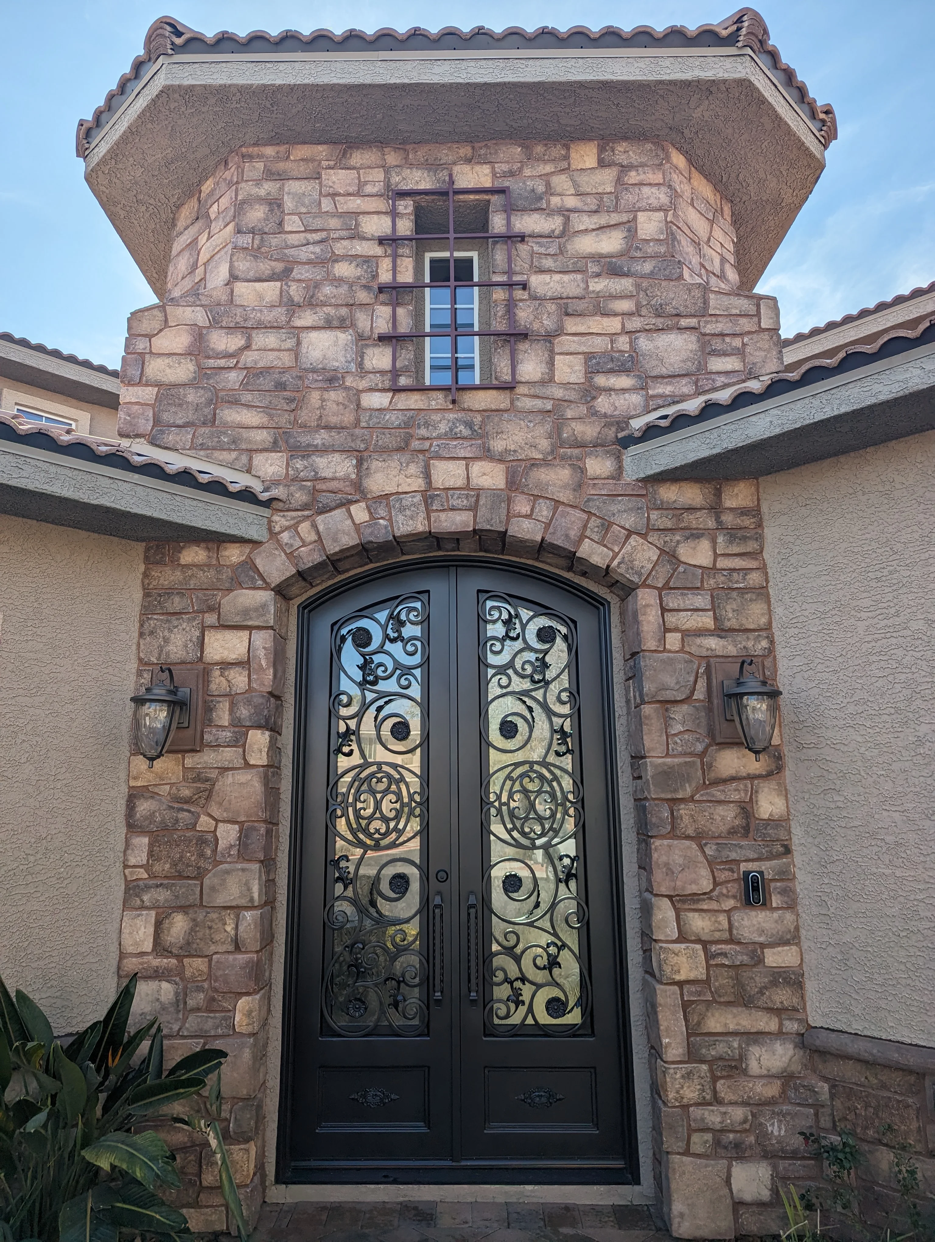 Stone masonry entry tower with black wrought iron doors and decorative tile roof