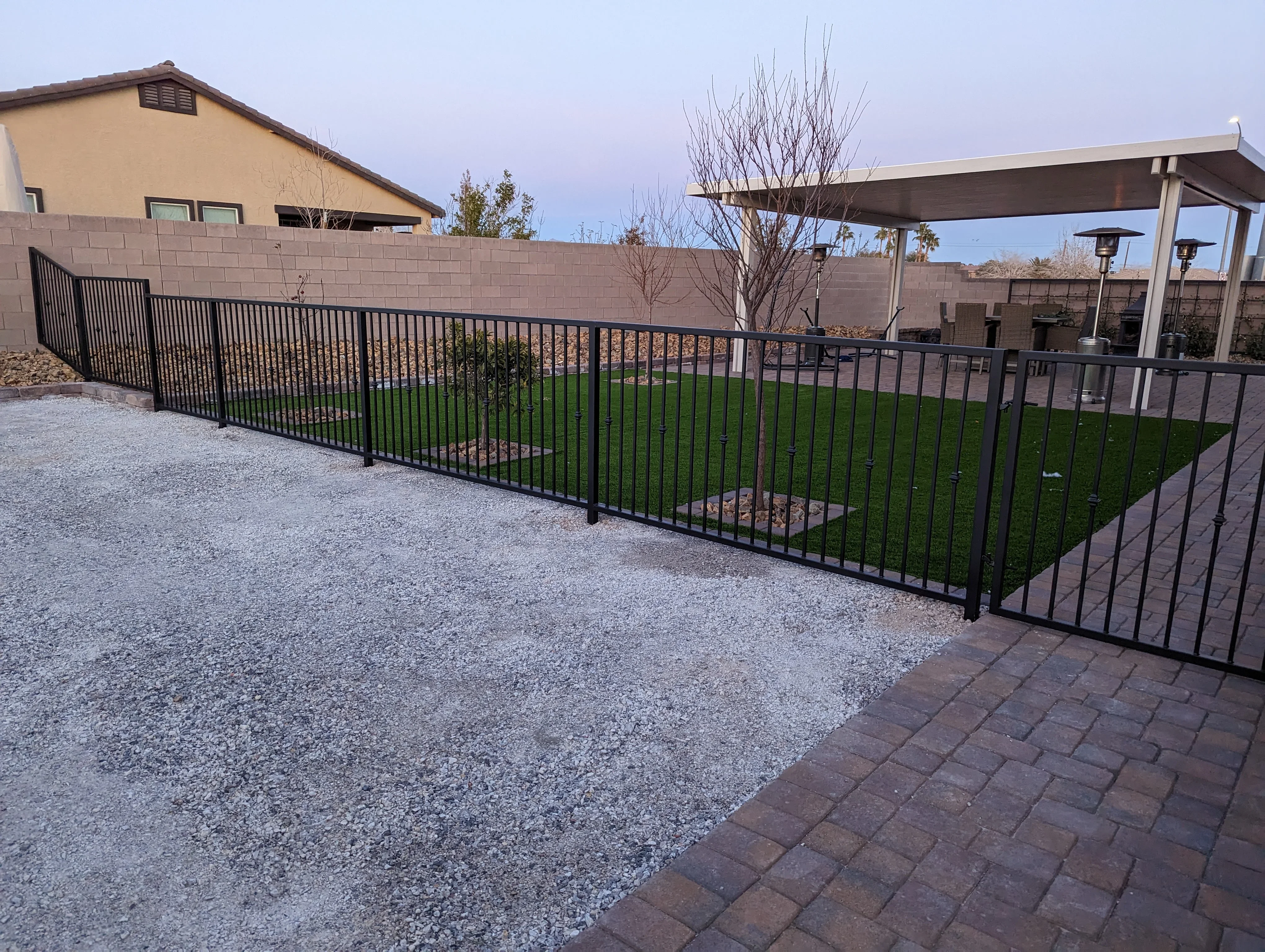 Black metal fence surrounding artificial turf yard with patio pergola and gravel landscaping