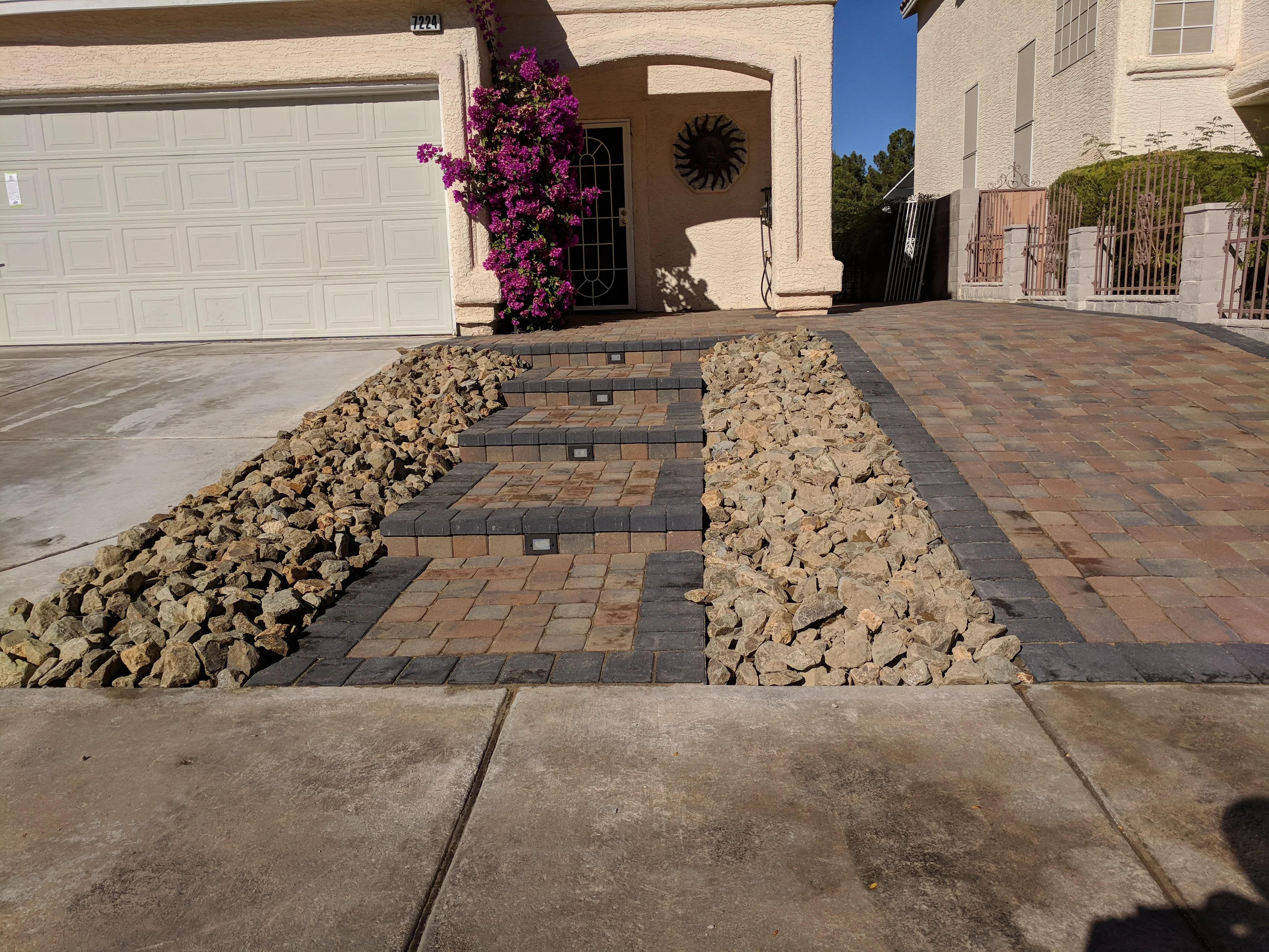 Paver driveway with geometric pattern and decorative rock borders leading to home entrance