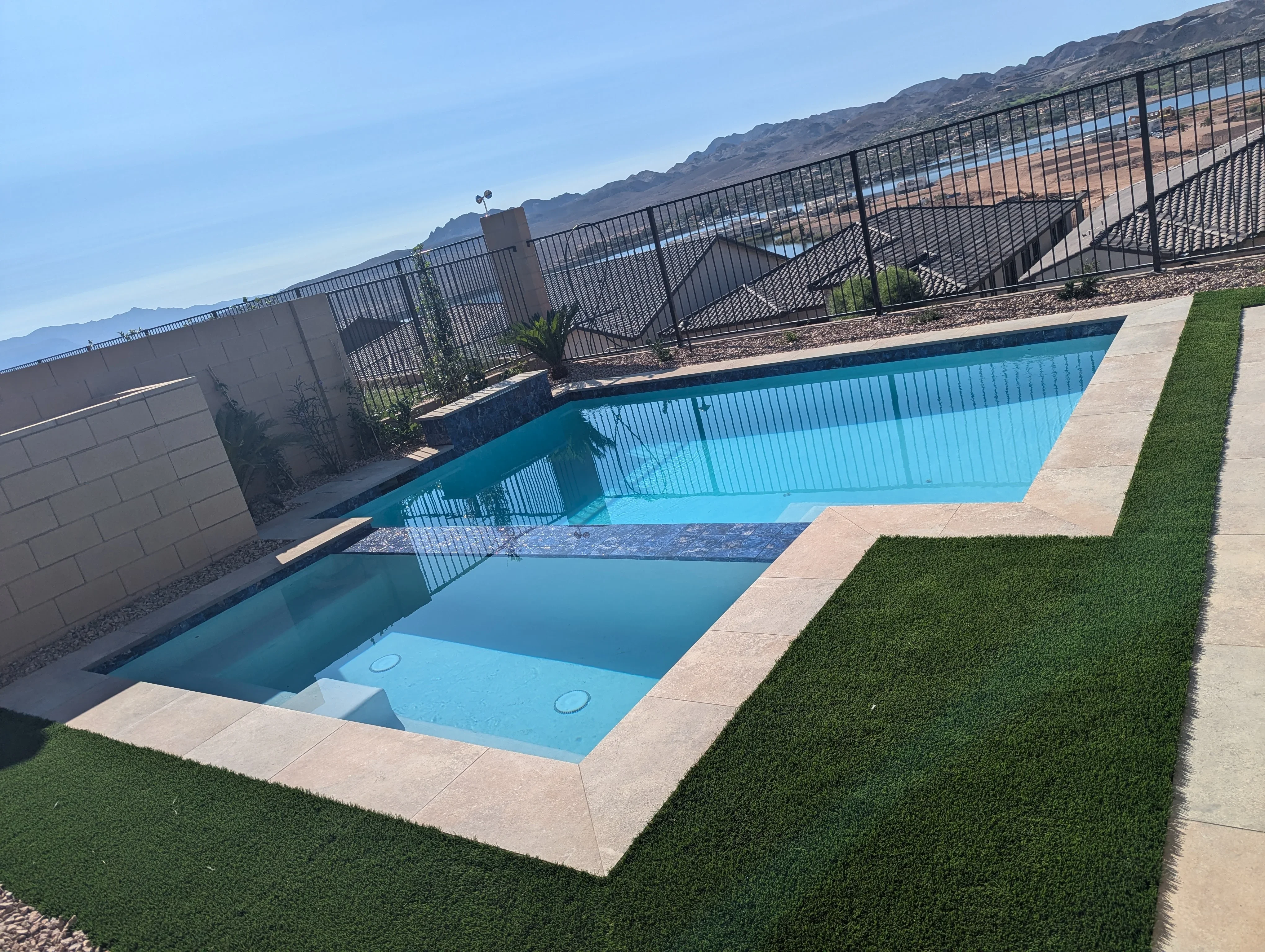 Modern backyard with two pools, concrete patio, artificial turf, and black metal fencing overlooking mountains