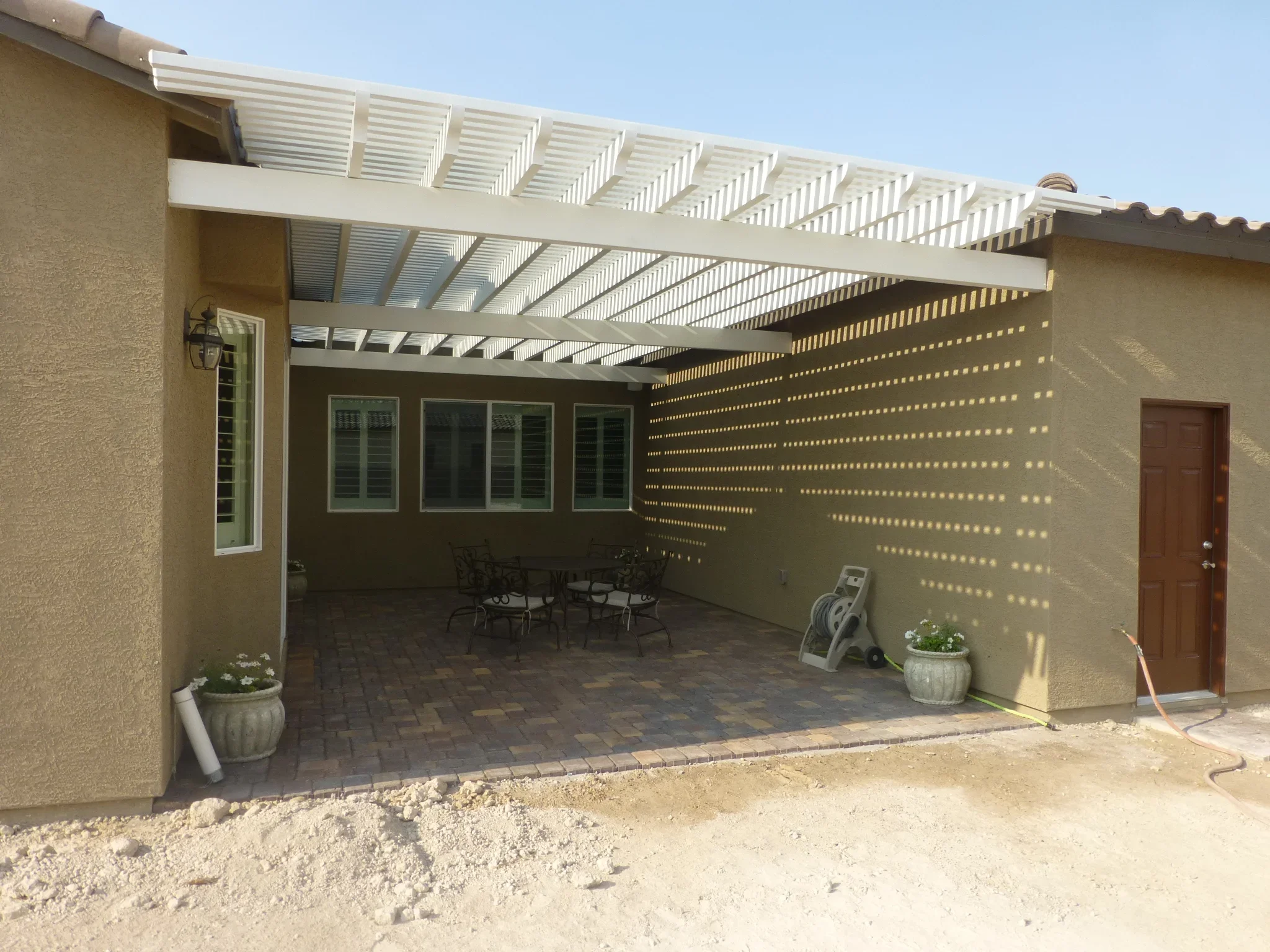 White pergola with louvers over brick paver patio and glass doors